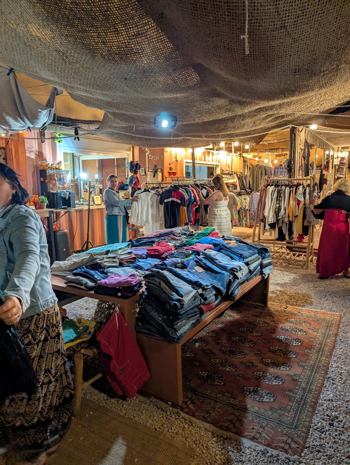 Intérieur de la friperie Pause Vintage le soir : portants de vêtements vintage et table de jeans pliés